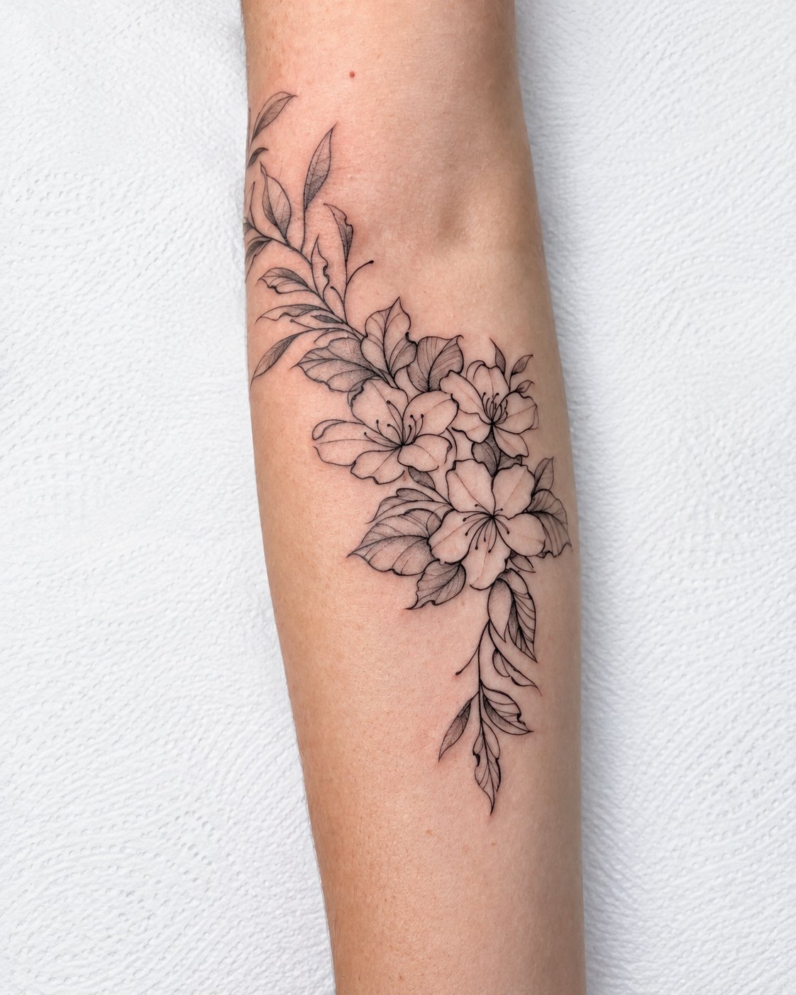 Tatuagem floral em fineline no antebraço, com flores e folhas em traço delicado